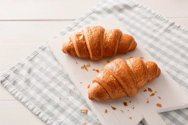 Board with tasty croissants on table
