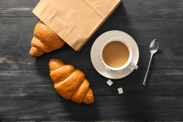 Bolsa de papel con sabrosos croissants y taza de café sobre mesa de madera —  Fotos de Stock