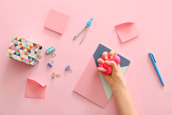 Mão espremendo bola de estresse e artigos de papelaria sobre fundo de cor — Fotografia de Stock