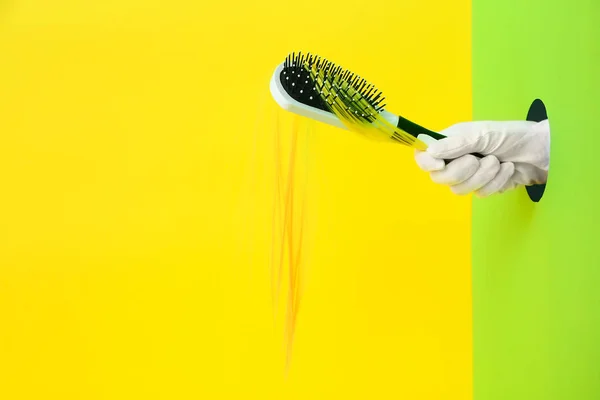 Mão feminina segurando escova com fio de cabelo no fundo de cor — Fotografia de Stock