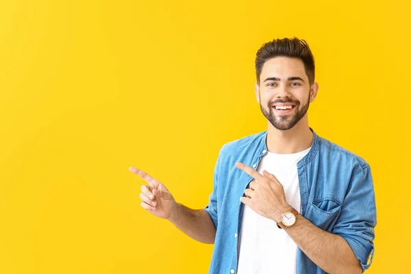 Handsome young man pointing at something on color background — Stock Photo, Image