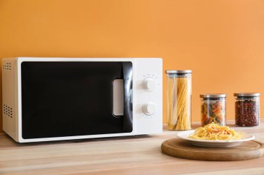 Plate with tasty pasta and microwave oven in kitchen