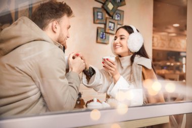 Happy young couple sitting in cafe, view through glass window