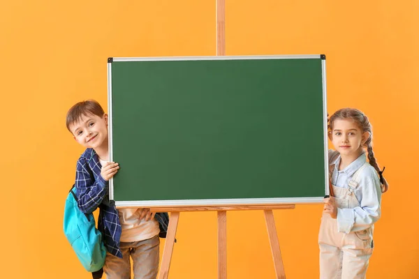 Kleine Schüler in der Nähe der Tafel auf farbigem Hintergrund — Stockfoto