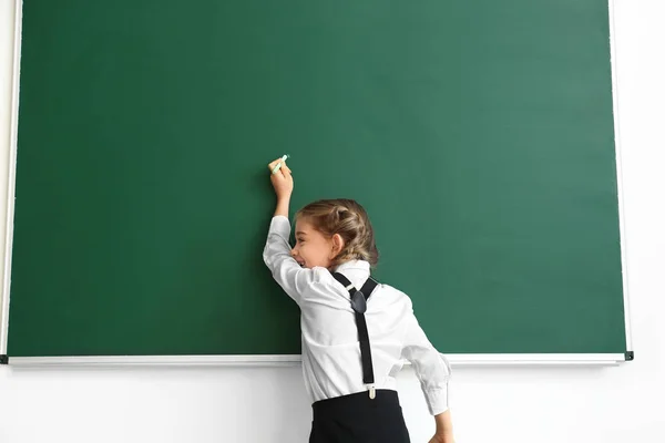 Schoolmeisje schrijven op schoolbord in de klas — Stockfoto
