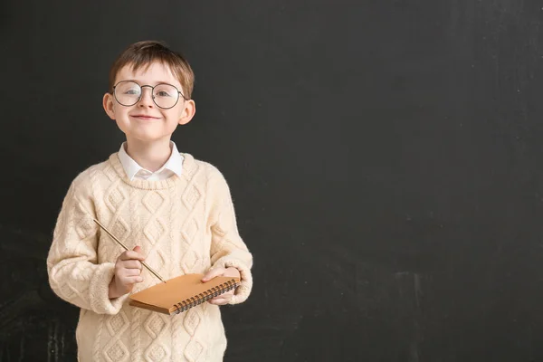 Little schoolboy with notebook near blackboard in classroom — Stok fotoğraf
