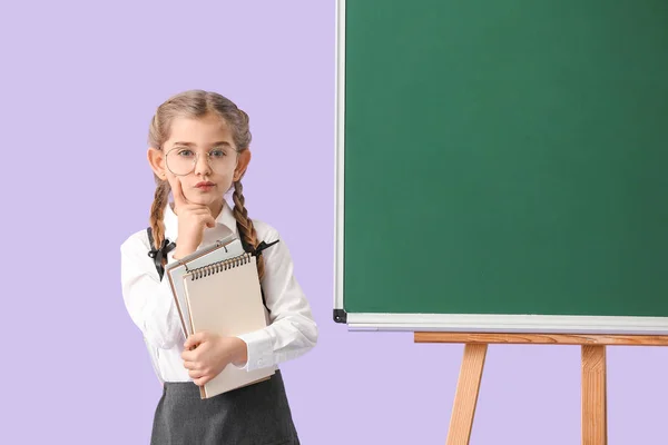 Klein schoolmeisje in de buurt van schoolbord op kleur achtergrond — Stockfoto