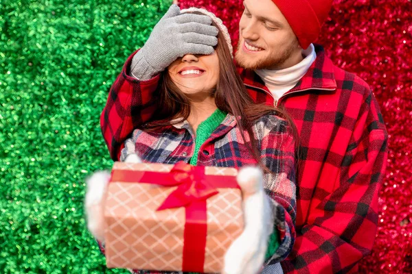 Young man covering eyes of her girlfriend with gift on color background — Stock Photo, Image