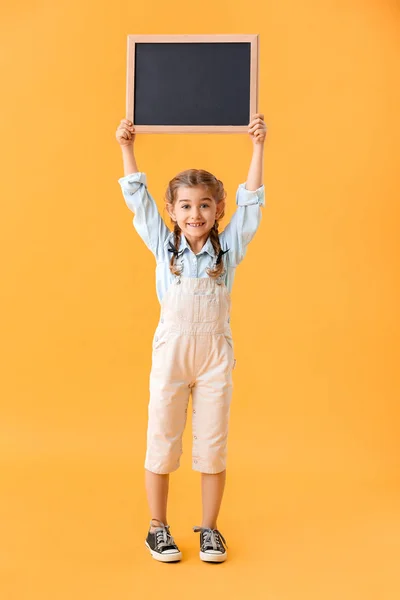 Little schoolgirl with chalkboard on color background — Stock Photo, Image