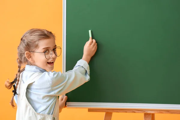 Kleine Schülerin schreibt auf Tafel vor farbigem Hintergrund — Stockfoto