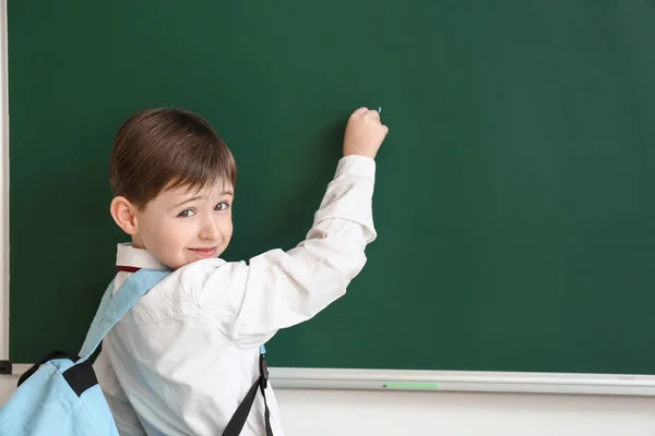 Pequeno estudante escrevendo em quadro negro em sala de aula — Fotografia de Stock