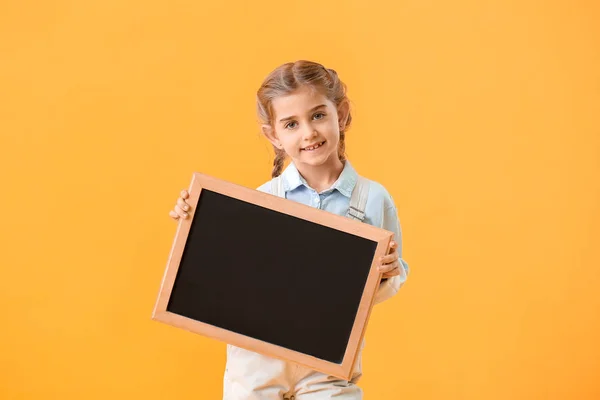 Kleines Schulmädchen mit Kreidetafel auf farbigem Hintergrund — Stockfoto