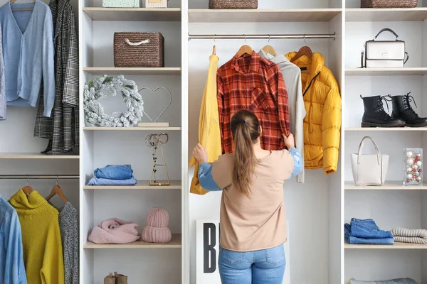 Mujer eligiendo ropa de invierno cerca de armario — Foto de Stock