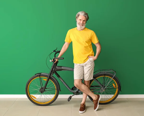 Stílusos idős férfi kerékpárral közel színes fal — Stock Fotó