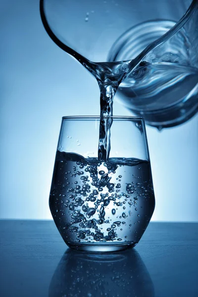 Pouring of fresh water in glass on color background — Stock Photo, Image