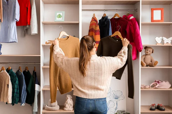 Mujer eligiendo ropa de invierno cerca de armario — Foto de Stock