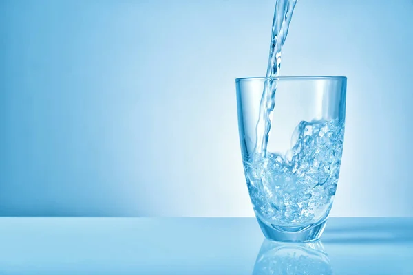 Pouring of fresh water into glass on color background — 스톡 사진