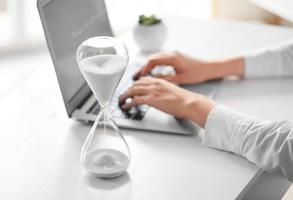Hourglass and woman working on laptop at table in office