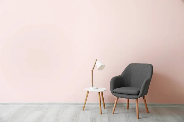 Poltrona elegante com mesa e lâmpada perto da parede de cor no quarto — Fotografia de Stock