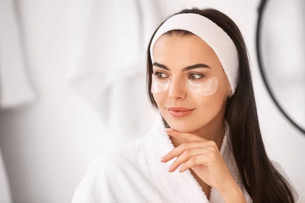 Beautiful young woman with under-eye patches in bathroom — Stock Photo, Image