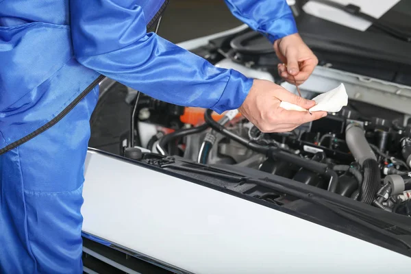 Male mechanic checking level of oil in car engine