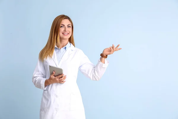 Portrait of female doctor with tablet computer showing something on color background — Stock Photo, Image