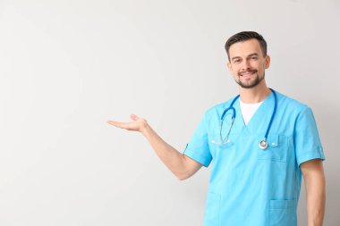 Portrait of male doctor showing something on light background