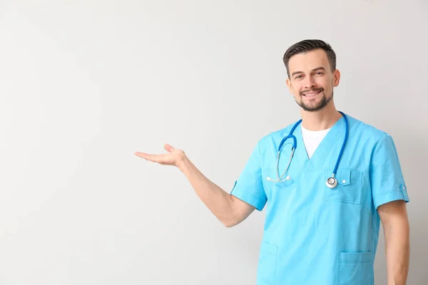 Portrait of male doctor showing something on light background — Stockfoto