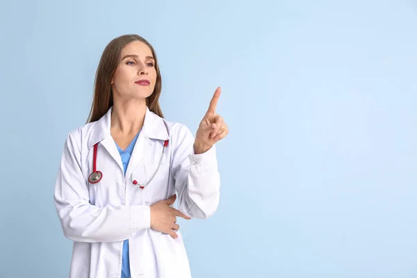 Portrait of female doctor showing something on color background — Stock Photo, Image