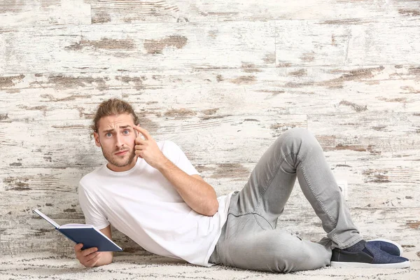 Pemuda Bingung dengan buku di dekat dinding kayu — Stok Foto