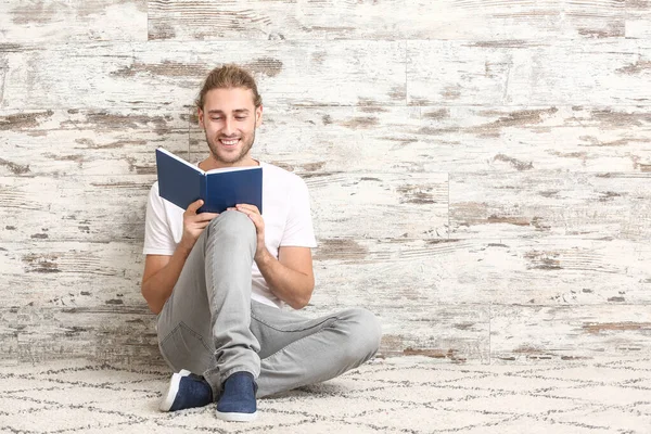 Hezký muž čtení knihy u dřevěné zdi — Stock fotografie