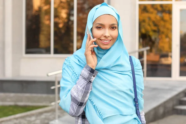 Beautiful young Muslim woman talking by phone outdoors — Stock Photo, Image