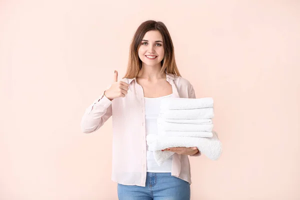 Beautiful young woman with laundry showing thumb-up on color background — ストック写真