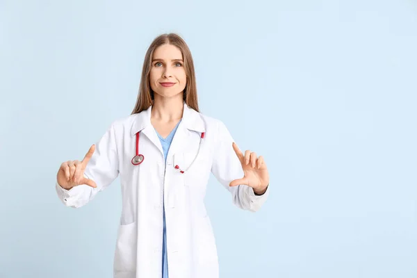 Portrait of female doctor showing something on color background — Stock Photo, Image