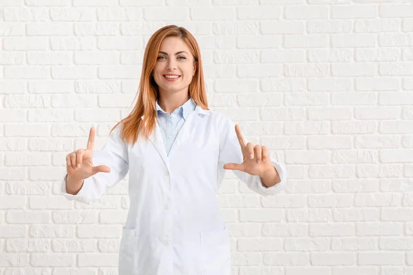 Portret van vrouwelijke arts tonen iets op witte baksteen achtergrond — Stockfoto
