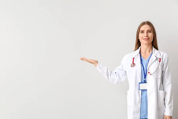 Portrait of female doctor showing something on light background — Stock Photo, Image