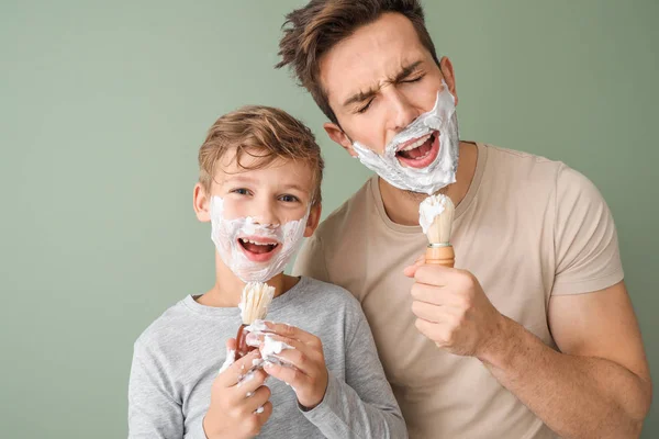 Забавный отец и его маленький сын бреются на цветном фоне — стоковое фото