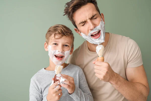 Divertente padre e il suo piccolo figlio rasatura contro colore sfondo — Foto Stock