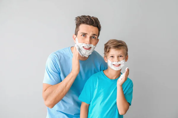 Père avec fils appliquant de la mousse à raser sur leurs visages sur fond clair — Photo