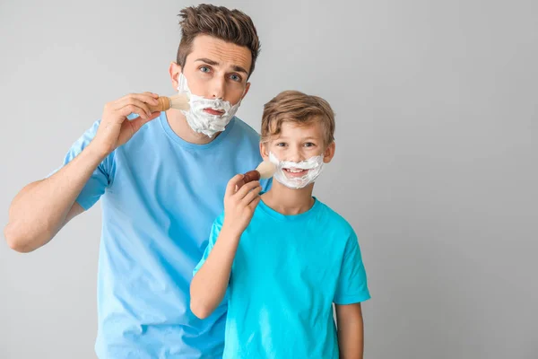 Padre con figlio che applica schiuma da barba sui loro volti sullo sfondo chiaro — Foto Stock