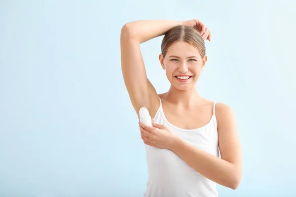 Hermosa mujer joven usando desodorante sobre fondo de color — Foto de Stock