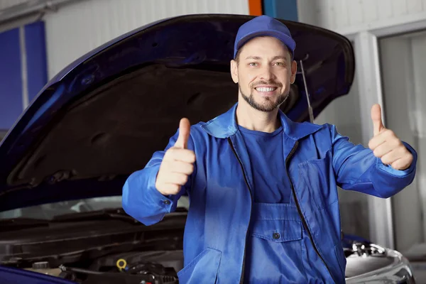 Manlig mekaniker visar tummen upp gest nära bilen i servicecenter — Stockfoto