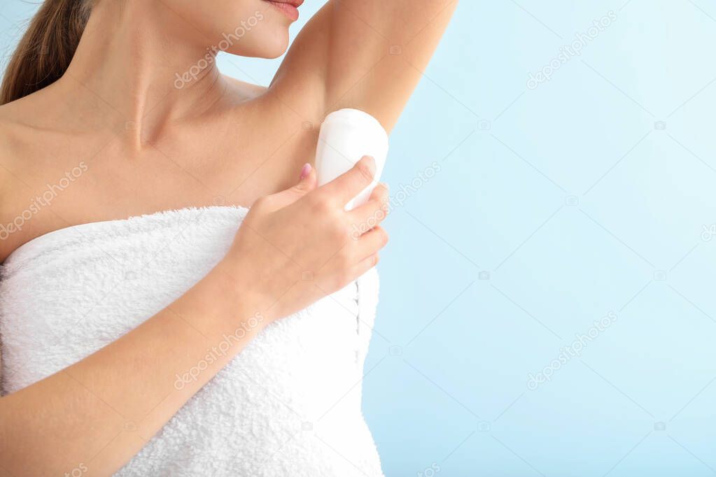 Beautiful young woman using deodorant on color background, closeup