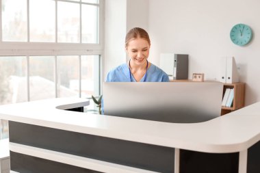 Young female receptionist working at desk in clinic clipart