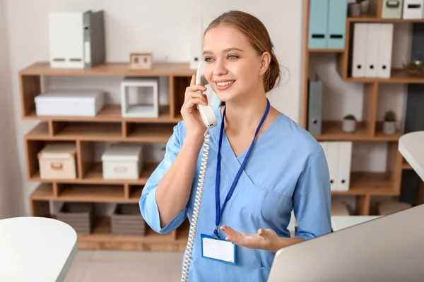 Молодая секретарша разговаривает по телефону за столом в клинике — стоковое фото