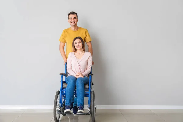 Mujer joven discapacitada en silla de ruedas y su marido cerca de la pared de luz — Foto de Stock