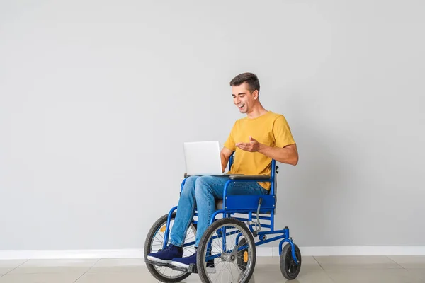 Joven discapacitado en silla de ruedas y con portátil cerca de la pared de luz — Foto de Stock