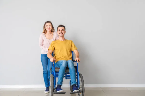 Handicapped young man in wheelchair and his wife near light wall — Stock Photo, Image