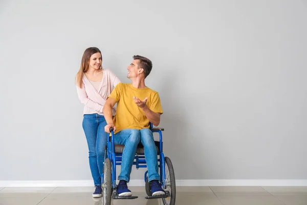 Joven discapacitado en silla de ruedas y su esposa cerca de la pared de luz — Foto de Stock