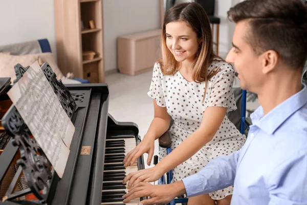 Young woman in wheelchair teaching man to play piano — Stock Photo, Image